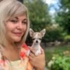 Breeder smiling while holding Pretty Penny Teacup Chihuahua in a beautiful garden.