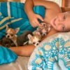 Brandon holding Pretty Penny Teacup Chihuahua and her siblings while relaxing on a bed.